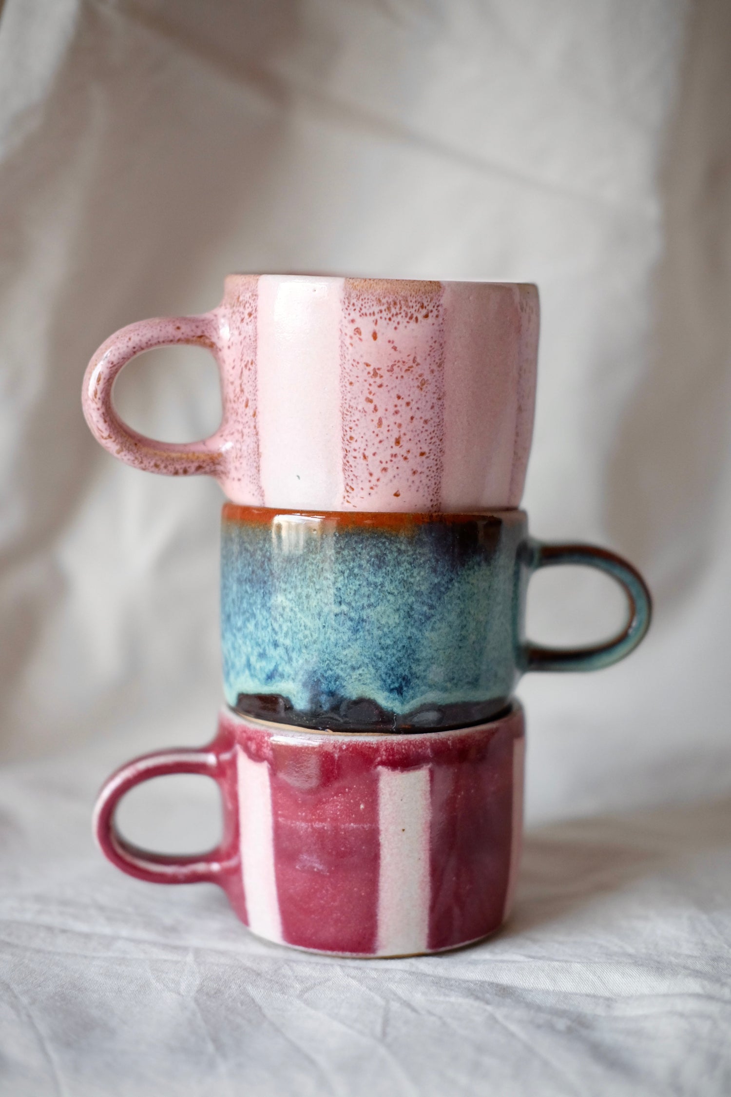 a stack of 3 mugs in varying colours of blue and pink stripes